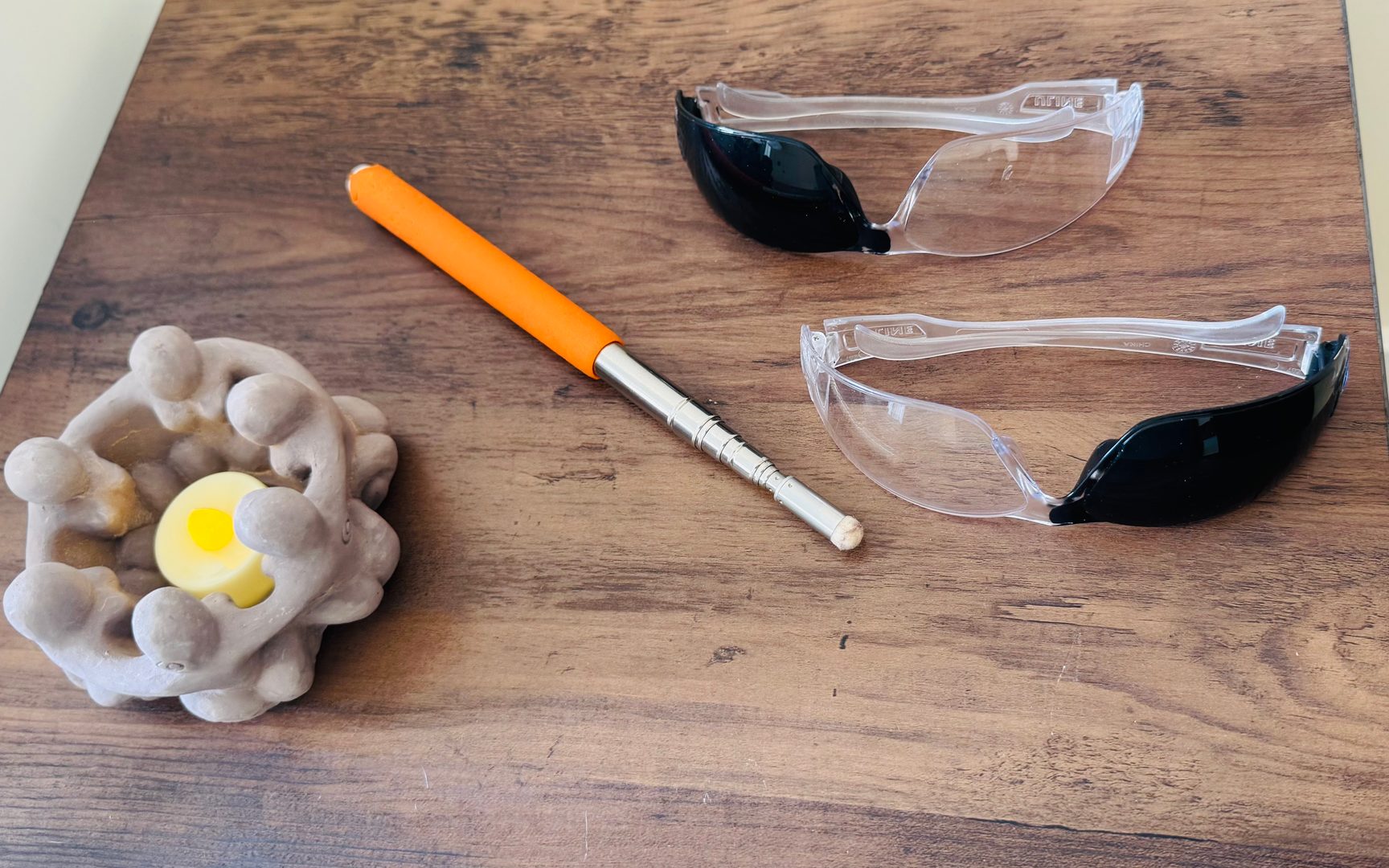 A Brainspotting pointer with an orange grip and a pair of Brainspotting glasses on a dark wood table, beside a lit candle