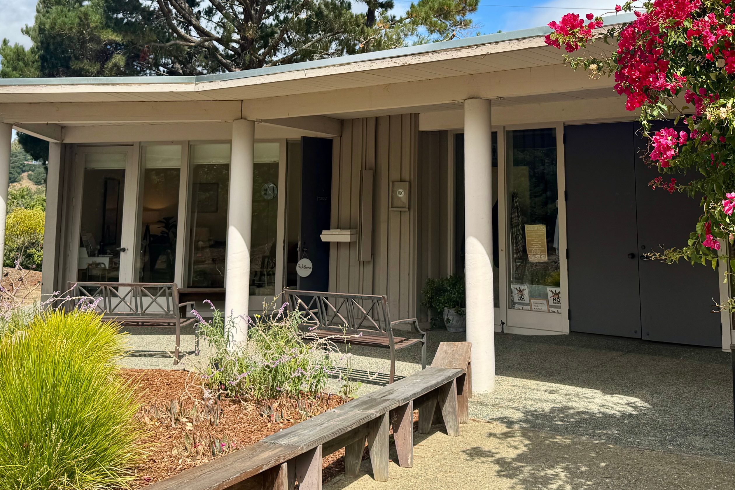 The covered porch outside the office: two benches under the roofline beside the entrance, with planting in front