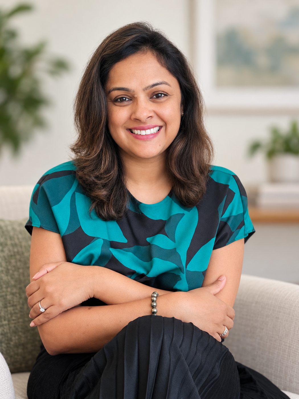 Tina Aggarwal seated and smiling at the camera, in a teal and black patterned top, in a light room
