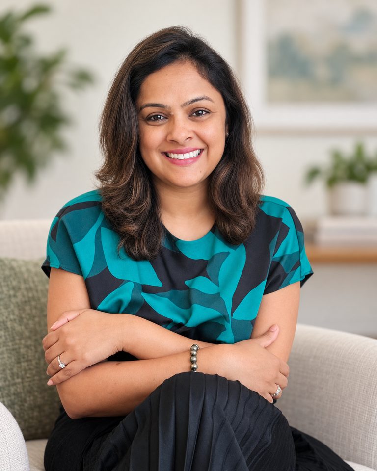 Tina Aggarwal seated and smiling at the camera, in a teal and black patterned top, in a light room
