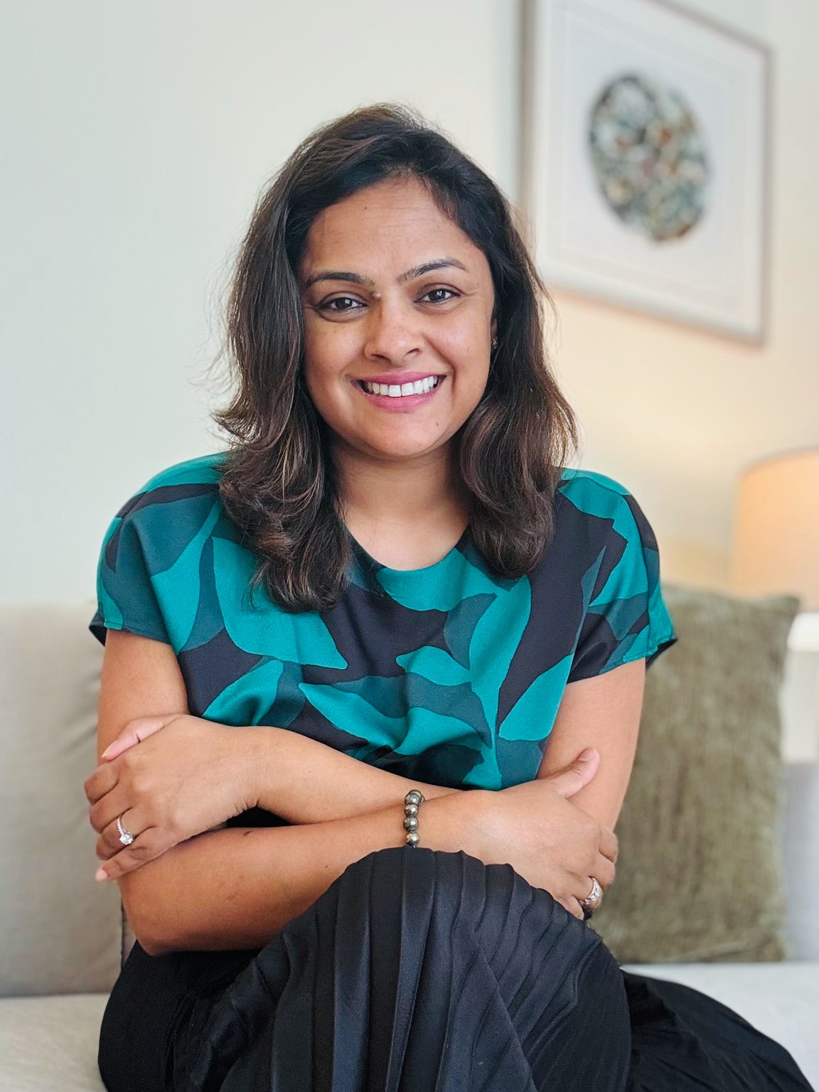 Tina Aggarwal seated on the sofa in her therapy office, arms folded, smiling