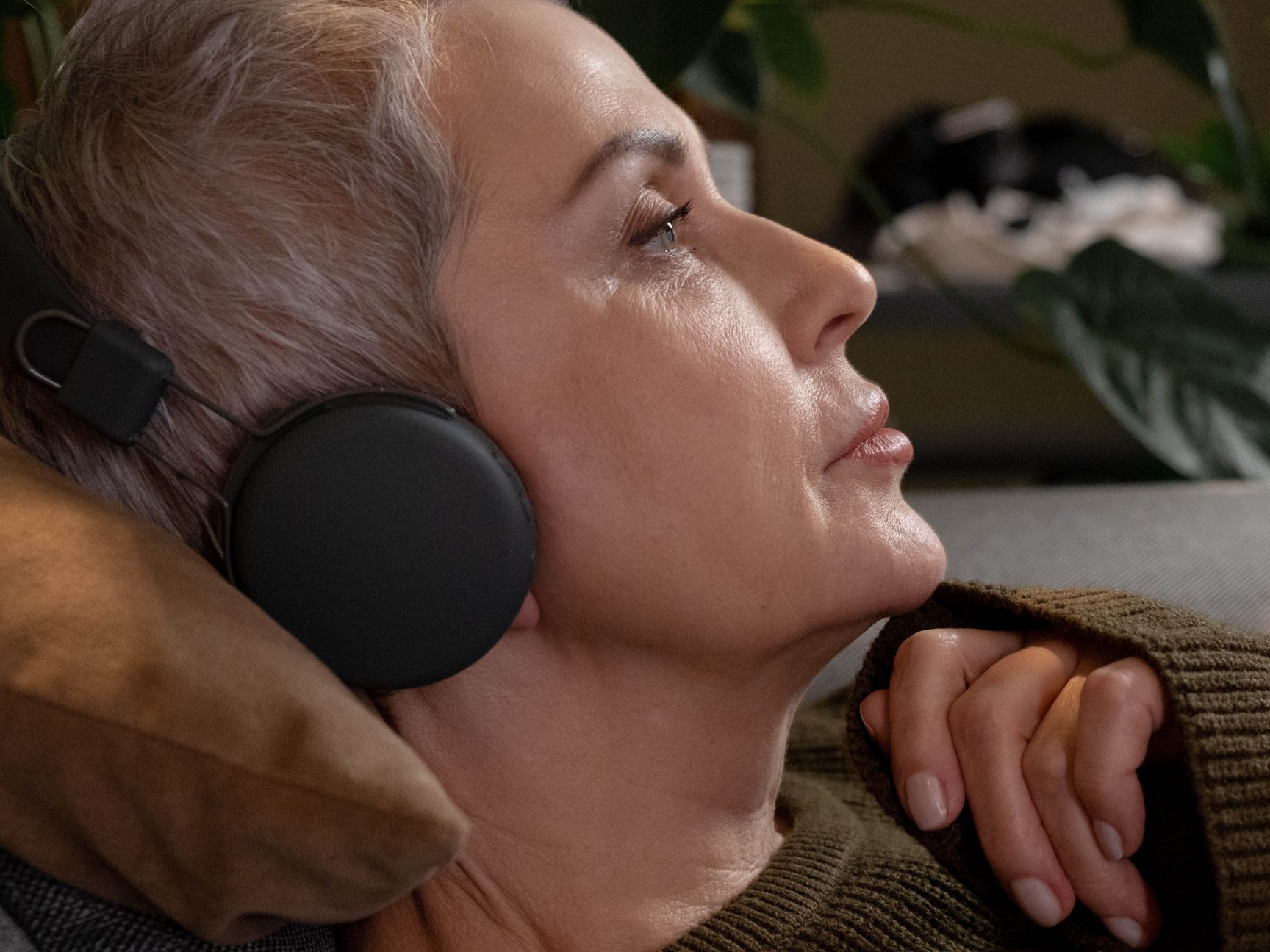 A woman reclining against a cushion in over-ear headphones, eyes open, her chin resting on her hand